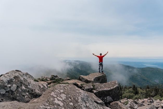 Turysta na szczycie góry cieszy się widokiem z lotu ptaka, unosząc ręce ponad chmury Góra Pidan