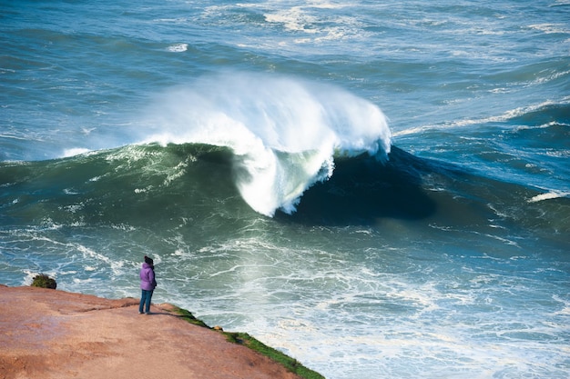 Turysta oglądający duże fale w Nazare, Portugalia. Sezon wielkich fal trwa tu od listopada do marca