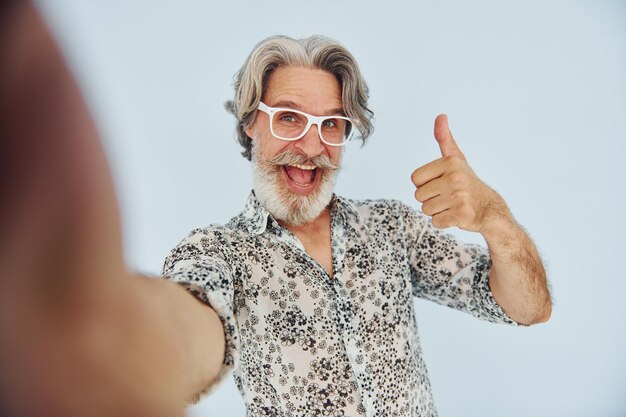 Turysta robi selfie Starszy stylowy nowoczesny mężczyzna z siwymi włosami i brodą w pomieszczeniu