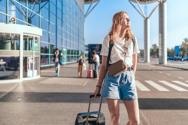 Turysta Travelwoman Z Plecakiem I Walizką Na Bagaż Podręczny Stojący W Pobliżu Terminalu Międzynarodowego Lotniska, Czekając Na Wejście Na Pokład. Koncepcja Aktywnego Stylu życia