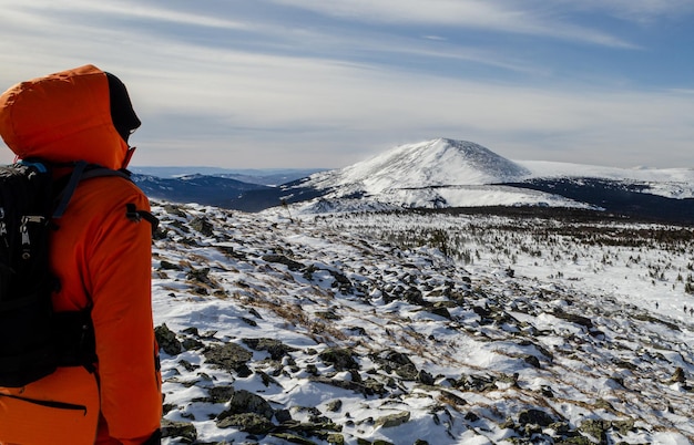 Turysta w pomarańczowej kurtce z plecakiem na pierwszym planie patrzy w dal. Zimowa kraina