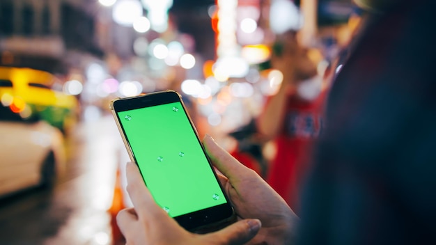 Turystka trzymająca smartfon z zielonym ekranem, stojąca na ulicy w nocy