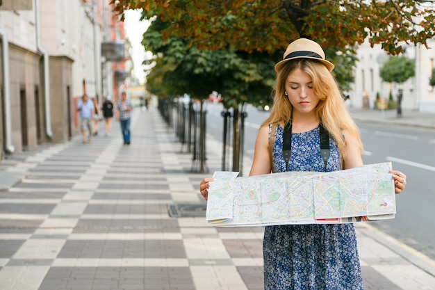 Turystka w kapeluszu z mapą podróżuje przez nieznane miasto.