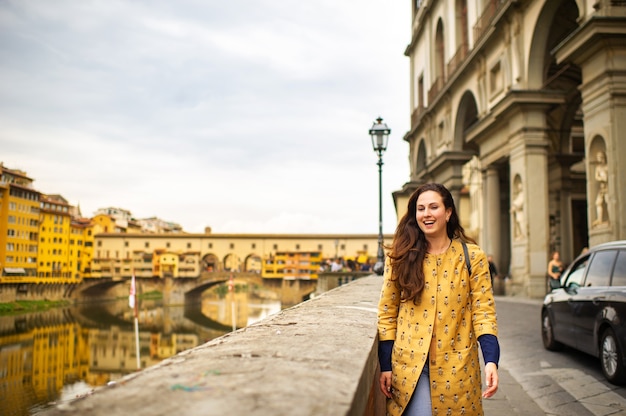 Turystka w pomarańczowym płaszczu szczęśliwie spaceruje po nasypie we Florencji we Włoszech.