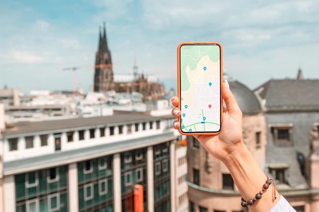 Turystka ze smartfonem, na ekranie którego znajduje się aplikacja z mapami i geolokalizacją na ulicach starego europejskiego miasta Katedra w Kolonii w tle