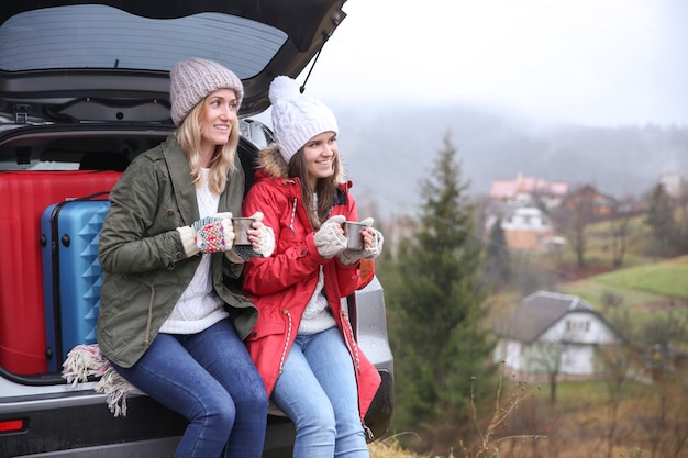 Turystki pijące gorącą herbatę w pobliżu samochodu na wsi