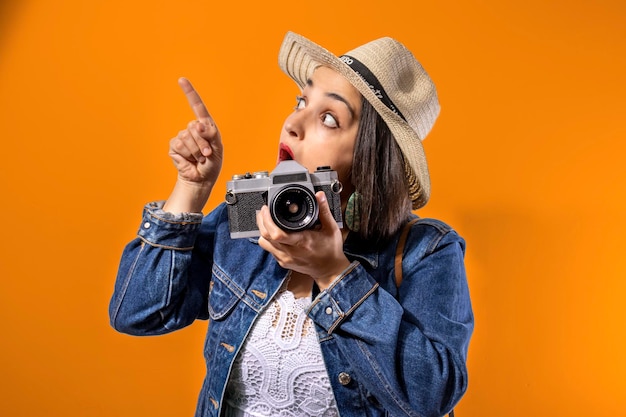 Turystyczna dziewczyna robi zdjęcia swoim retro aparatem koncepcja podróży pomarańczowym tłem