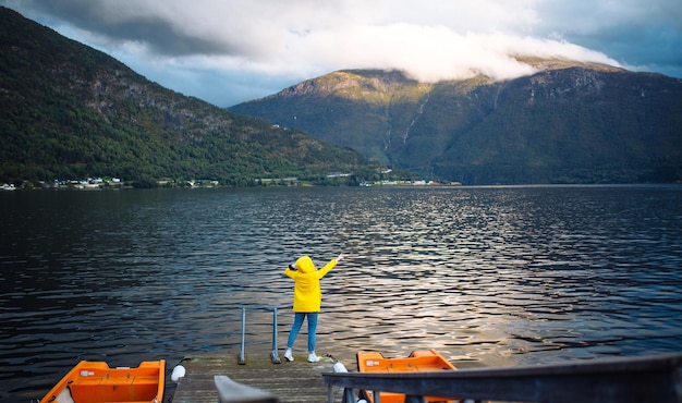 Turystyczna dziewczyna w żółtej kurtce pozuje na jeziorze w Norwegii Podróżująca przygoda stylu życia