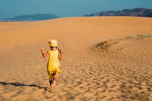 Turystyczna dziewczyna w żółtej sukience biegnie wzdłuż piaszczystej wydmy na pustyni Zabytki z podróży po wydmie Sarykum w Dagestanie