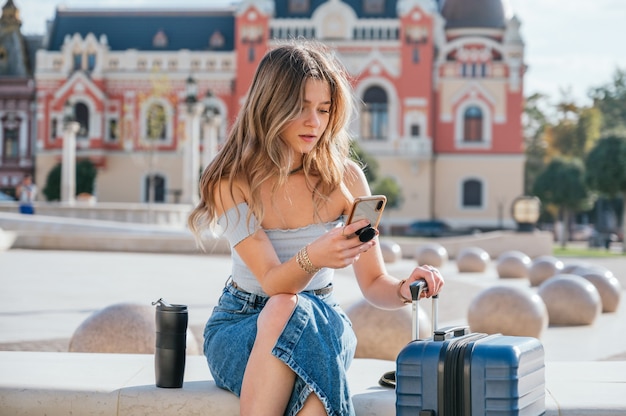 Turystyczna kobieta z jej walizką za pomocą swojego smartfona