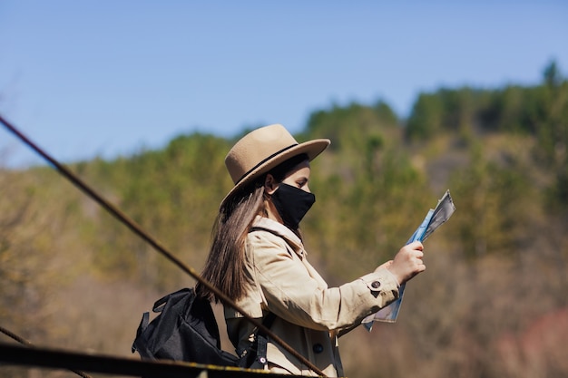 Turystyczna kobieta z maską ochronną stojącą z papierową mapą na moście wiszącym