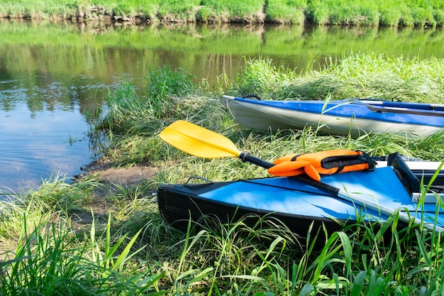 Zdjęcie turystyczne kajaki z wiosłami stoją latem nad brzegiem rzeki na wodnej wędrówce rafting na nadmuchiwanych i ramowych dwu- i trzyosobowych łódkach rodzinnych ekstremalna przygoda latem