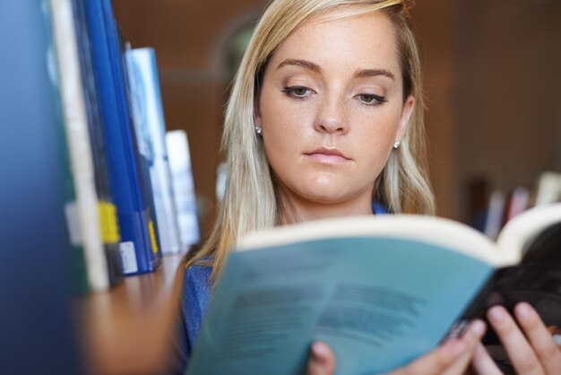 Zdjęcie twarz czytająca książkę lub kobieta w bibliotece na uniwersytecie, uczelni lub kampusie szkolnym dla przyszłej edukacji uczenie się na półce lub studentka z stypendium studiująca badania wiedzy lub informacje