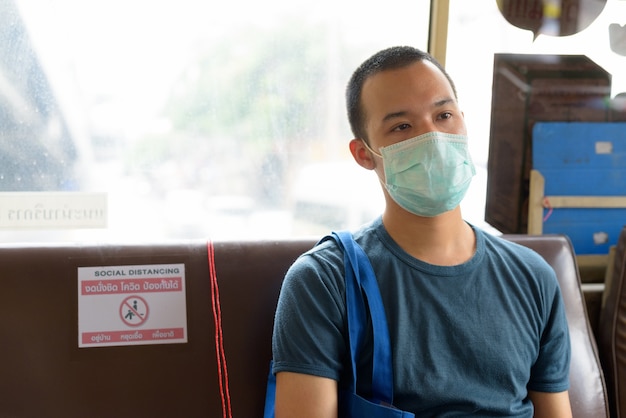 Twarz młodego mężczyzny Azji z maską, jazda autobusem z odległości