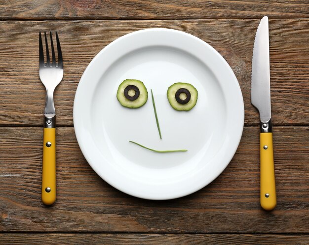 Zdjęcie twarz warzywna na talerzu z nożem i widelcem na drewnianym stole