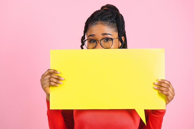 Twój tekst tutaj Podekscytowana dziewczyna afro trzymająca pustą pustą tablicę odizolowaną nad pastelową różową ścianą studia copyspace