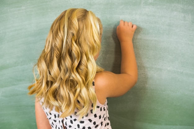 Tylni widok szkolnej dziewczyny writing na chalkboard w sala lekcyjnej