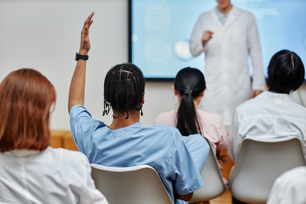 Tylny młody czarny lekarz podnoszący rękę na widowni na seminarium medycznym