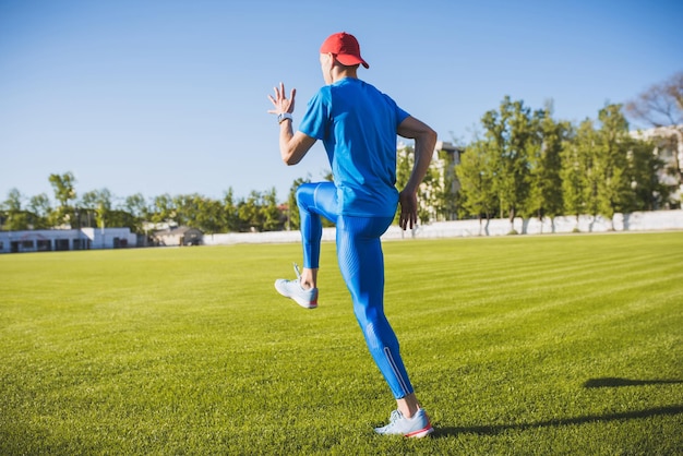 Tylny poziomy widok aktywnego młodego sportowca płci męskiej biegania i biegania samotnie wzdłuż zielonego trawnika piłkarskiego na stadionie podczas treningu w słoneczny dzień Sportowy styl życia i koncepcja ludzi