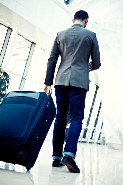 Tylny widok biznesmena niosącego bagaż idącego w kierunku ruchomych schodów w holu lotniska