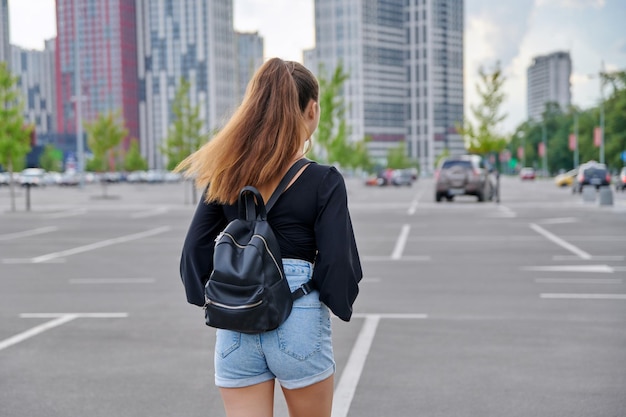 Tylny widok chodzić modną nastoletnią dziewczynę z plecakiem