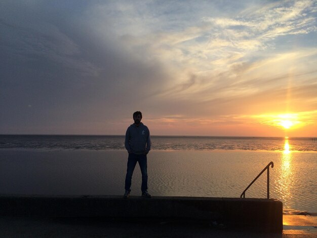 Tylny widok człowieka stojącego na plaży na tle nieba podczas zachodu słońca