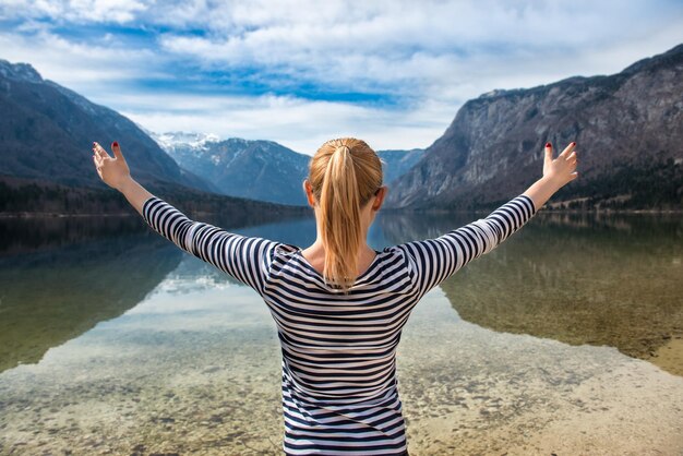 Zdjęcie tylny widok kobiety stojącej z wyciągniętymi rękami nad jeziorem na tle gór