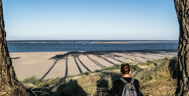 Zdjęcie tylny widok kobiety z plecakiem idącej po plaży na tle nieba w słoneczny dzień