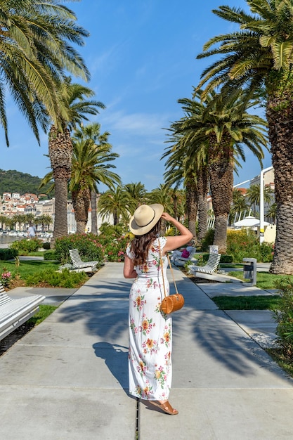 Zdjęcie tylny widok młodej kobiety ubranej w letnią sukienkę na promenadzie pod palmami
