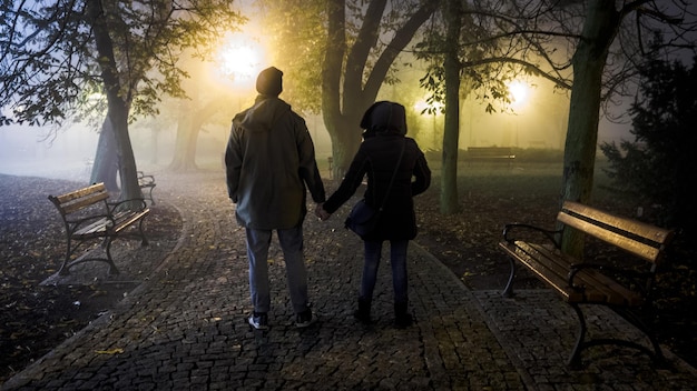 Zdjęcie tylny widok pary trzymającej się za ręce, stojącej na chodniku przeciwko drzewom