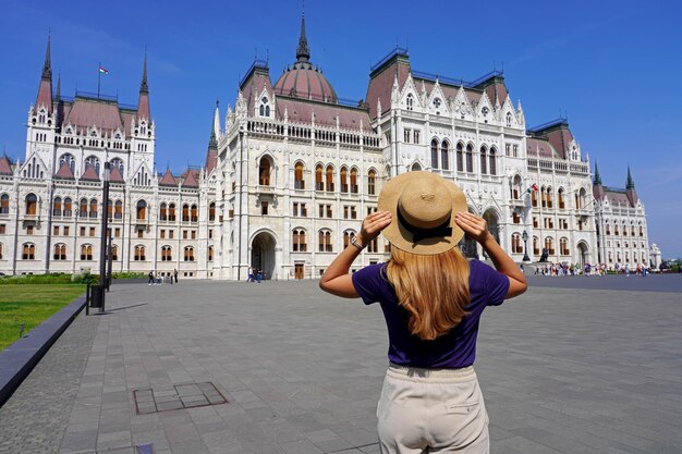 Zdjęcie tylny widok pięknej dziewczyny cieszącej się widokiem na budynek węgierskiego parlamentu w budapeszcie