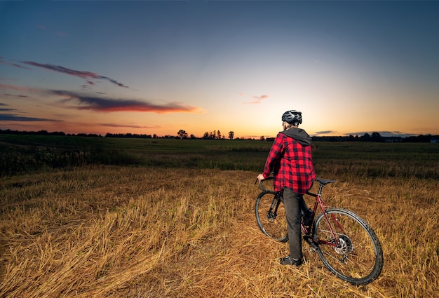 Tylny widok rowerzysty na rowerze żwirowym w polu o zachodzie słońca