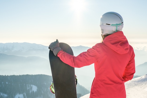 Zdjęcie tylny widok żeńska snowboarder pozycja z snowboard i cieszyć się góra krajobraz