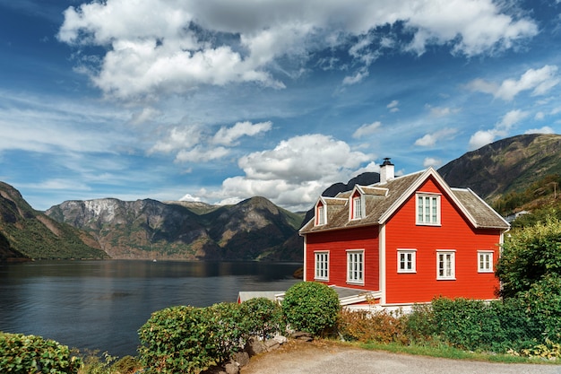 Typowy Norweski Czerwony Dom W Tle Malowniczego Fiordu. Piękny Krajobraz Norwegii Z Czerwonym Domem I Atmosferycznym Niebem.