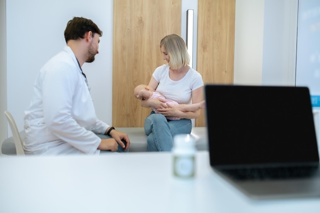 U lekarza. Blond mama rozmawia z pediatrą i trzyma swoje dziecko