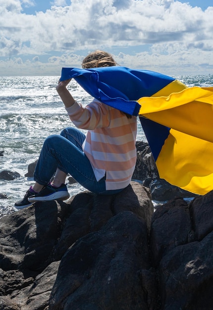 Uchodźczyni trzymająca flagę narodową Ukrainy siedząca nad oceanem