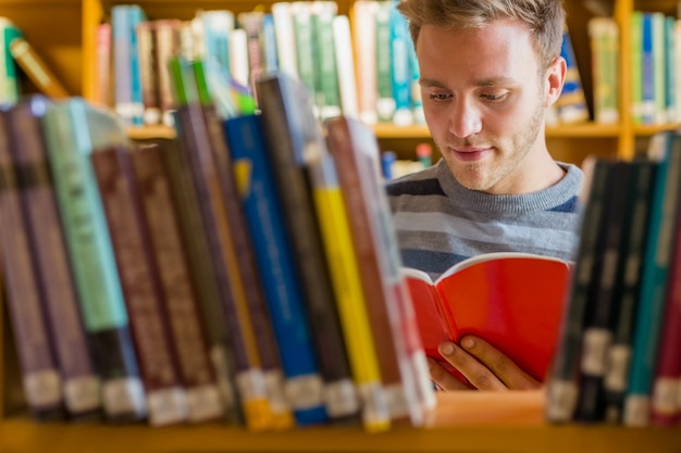 Uczeń czyta książkę wśród półek na książki w bibliotece