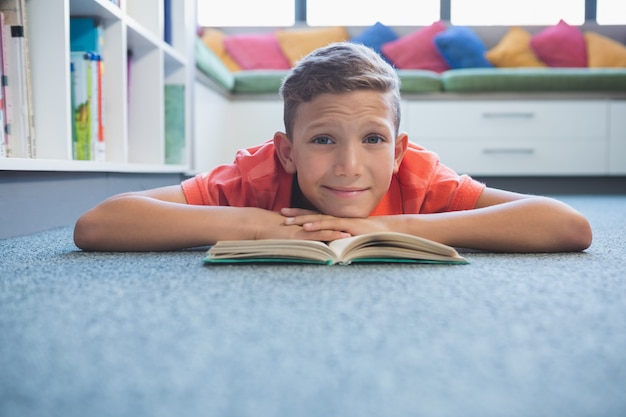 Uczeń, leżąc na podłodze i czytając książkę w bibliotece