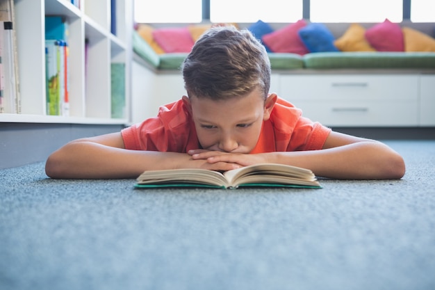 Uczeń, leżąc na podłodze i czytając książkę w bibliotece