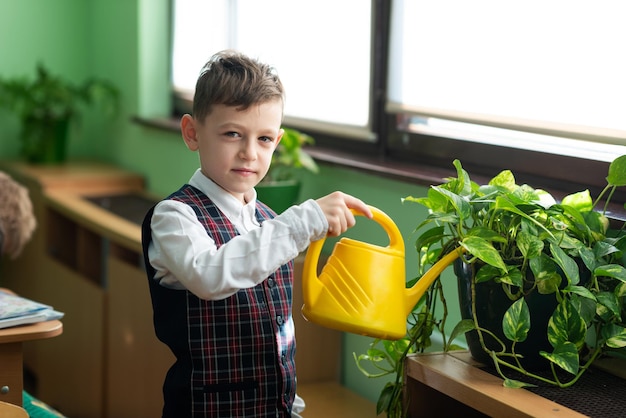 Uczeń podlewa kwiaty z żółtej konewki w klasie