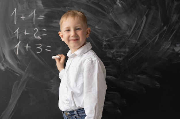 Uczeń stoi przy tablicy w klasie i pisze przykłady z matematyki. Chłopiec się uśmiecha. Pozytywny uczeń na lekcji. Powrót do szkoły. Lekcja matematyki w szkole podstawowej.