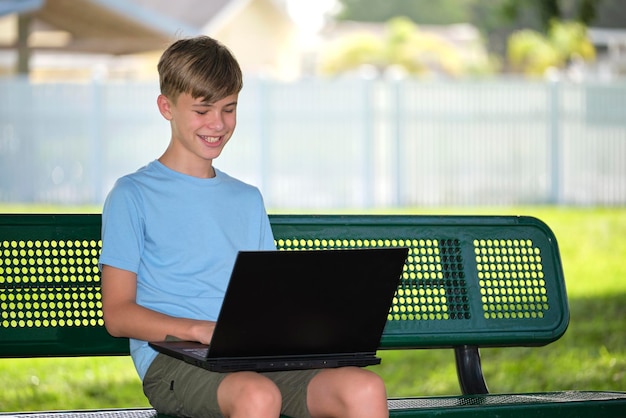 Uczeń studiujący na laptopie spoczywający na ławce w parku na świeżym powietrzu w letni dzień Zdalna edukacja podczas koncepcji kwarantanny