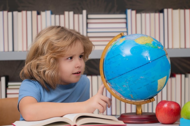 Uczeń szkoły patrząc na kulę ziemską w bibliotece lekcja geografii dziecko w wieku szkolnym studiujące w klasie w elem