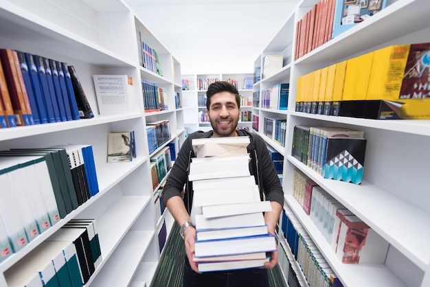 Uczeń trzymający mnóstwo książek w szkolnej bibliotece Ciężko pracujący i wytrwały