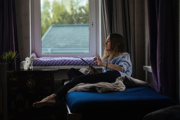 Uczennica komunikuje się i uczy w domu przy oknie na tablecie