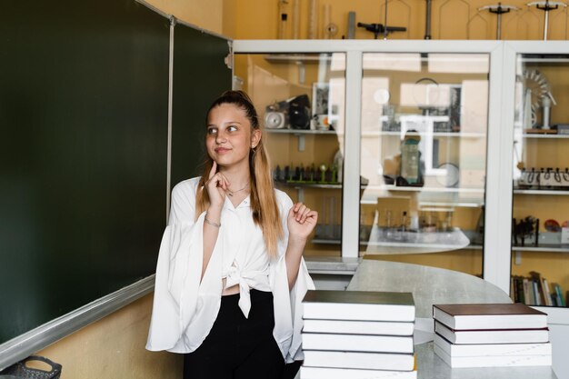 Uczennica myśli o lekcji i uśmiecha się Edukacja szkolna Dziecko w szkole z wieloma książkami przy tablicy