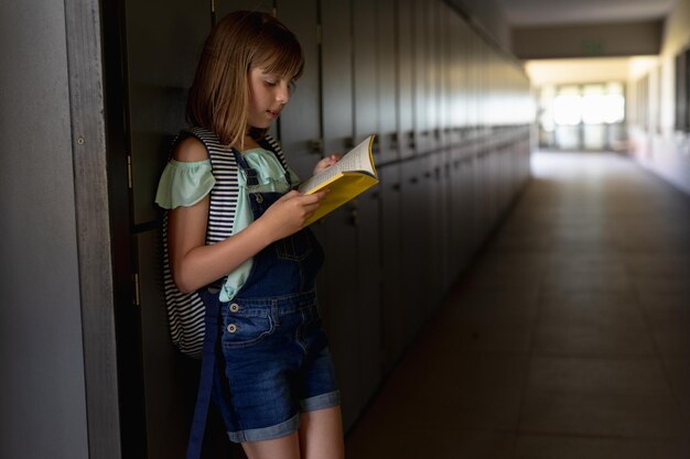 Zdjęcie uczennica oparta o ścianę w korytarzu na świeżym powietrzu, czytająca książkę w szkole podstawowej