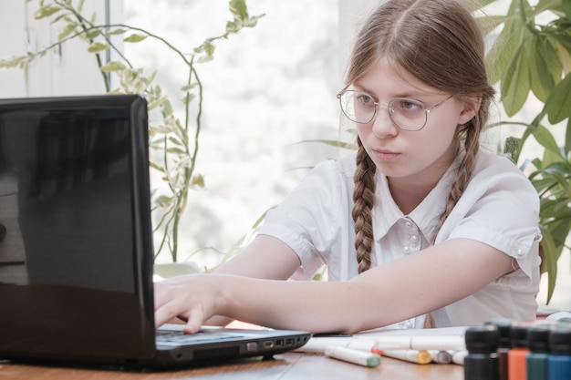 Uczennica samodzielna izolacja za pomocą laptopa do pracy domowej. Dziewczyna robi za pomocą cyfrowego tabletu, szukając informacji w Internecie podczas covid 19 lock down. Dystans społeczny, edukacja e-learningowa online