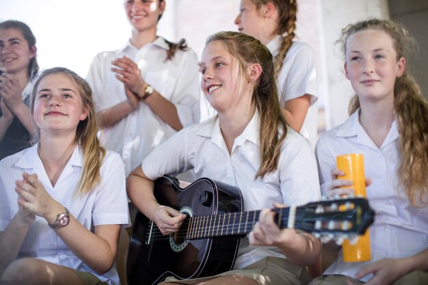 Zdjęcie uczennica szkoły średniej gra na gitarze z grupą przyjaciół ze szkoły na zewnątrz