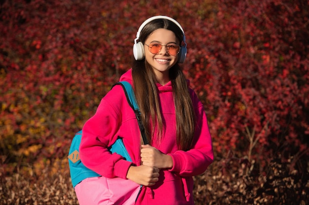uczennica w jesiennym parku na świeżym powietrzu z plecakiem idącym do szkoły w okularach przeciwsłonecznych i słuchawkach